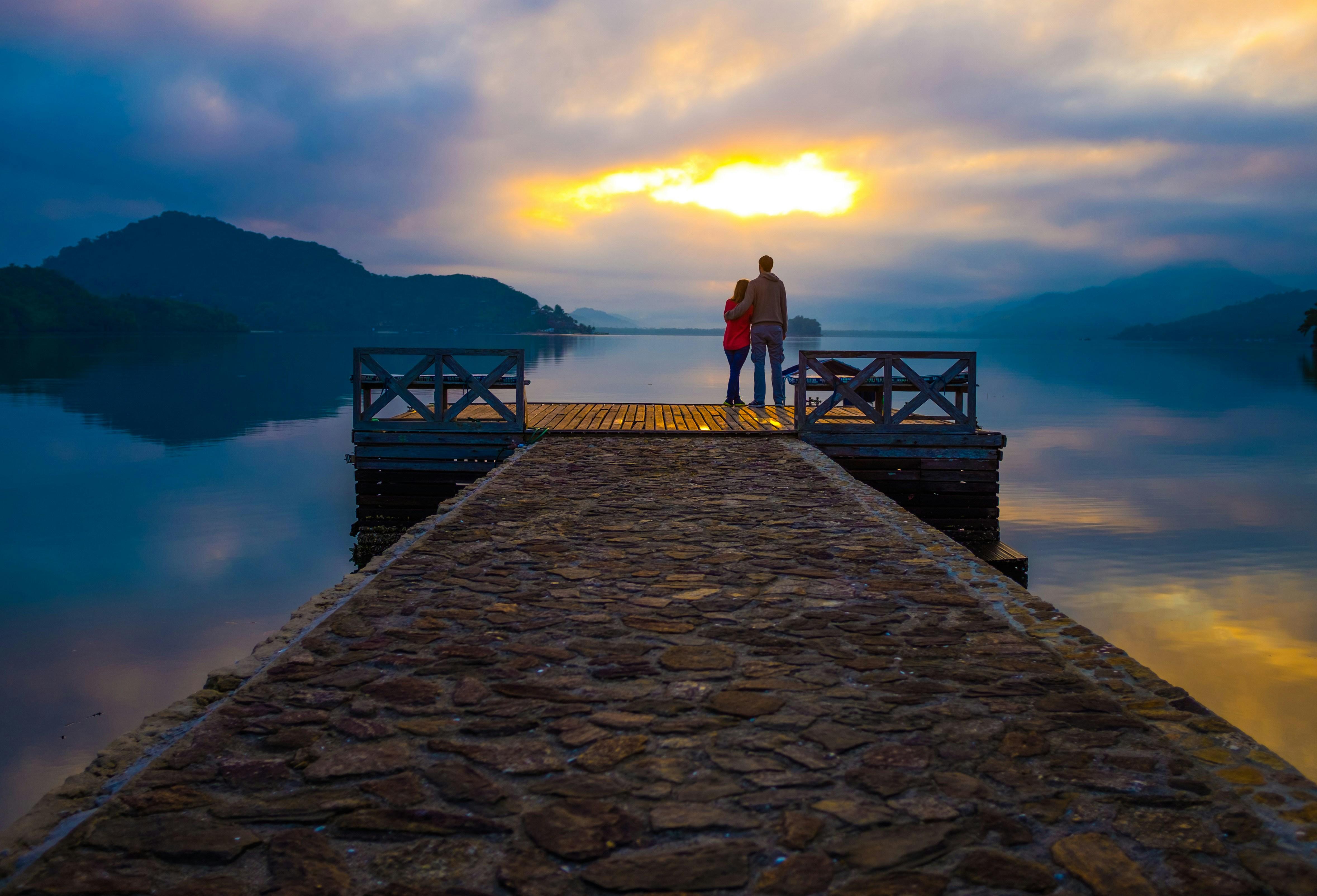 Couple standing together at the end of a pier at sunset