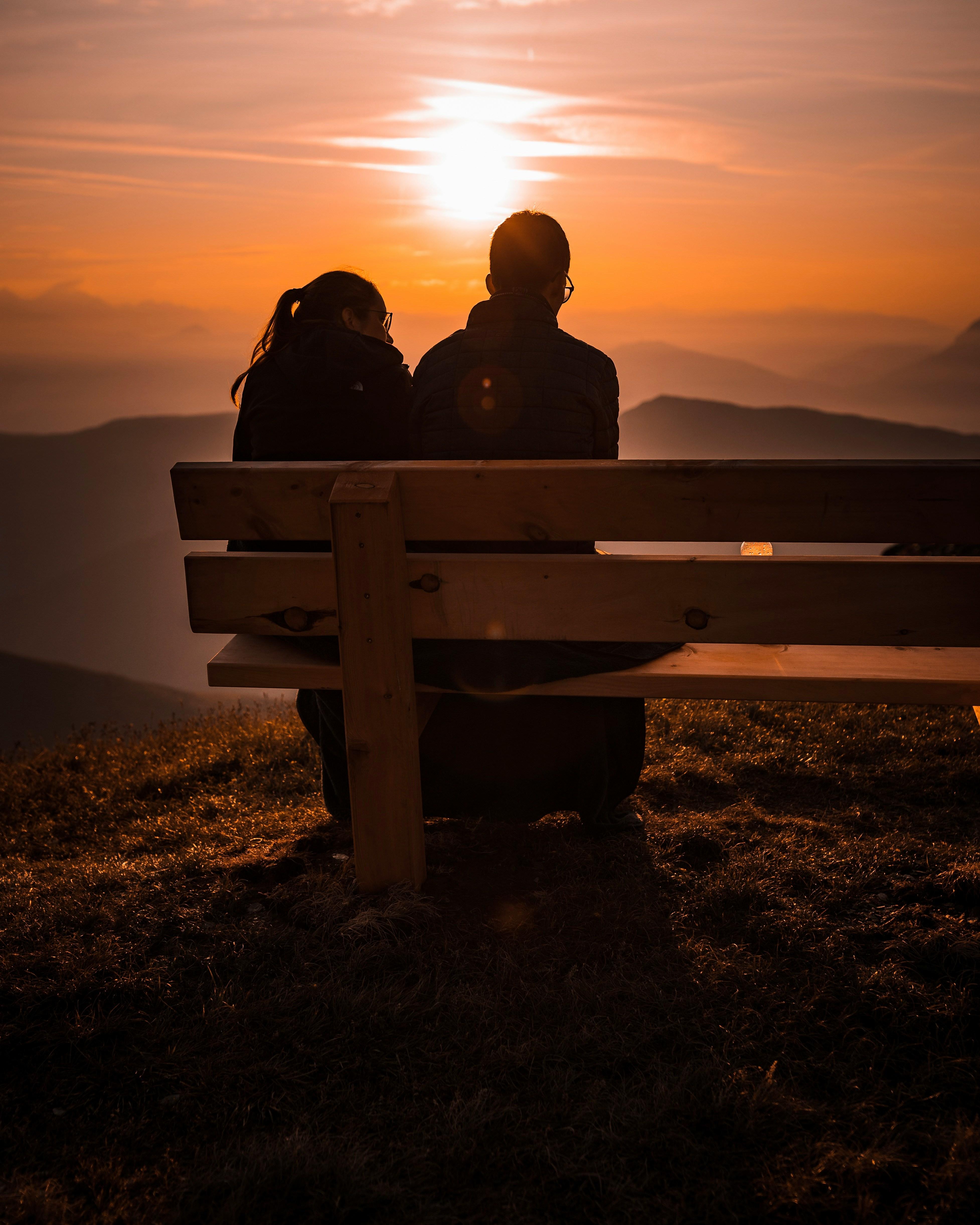 Couple sitting on a bench overlooking mountains at sunset