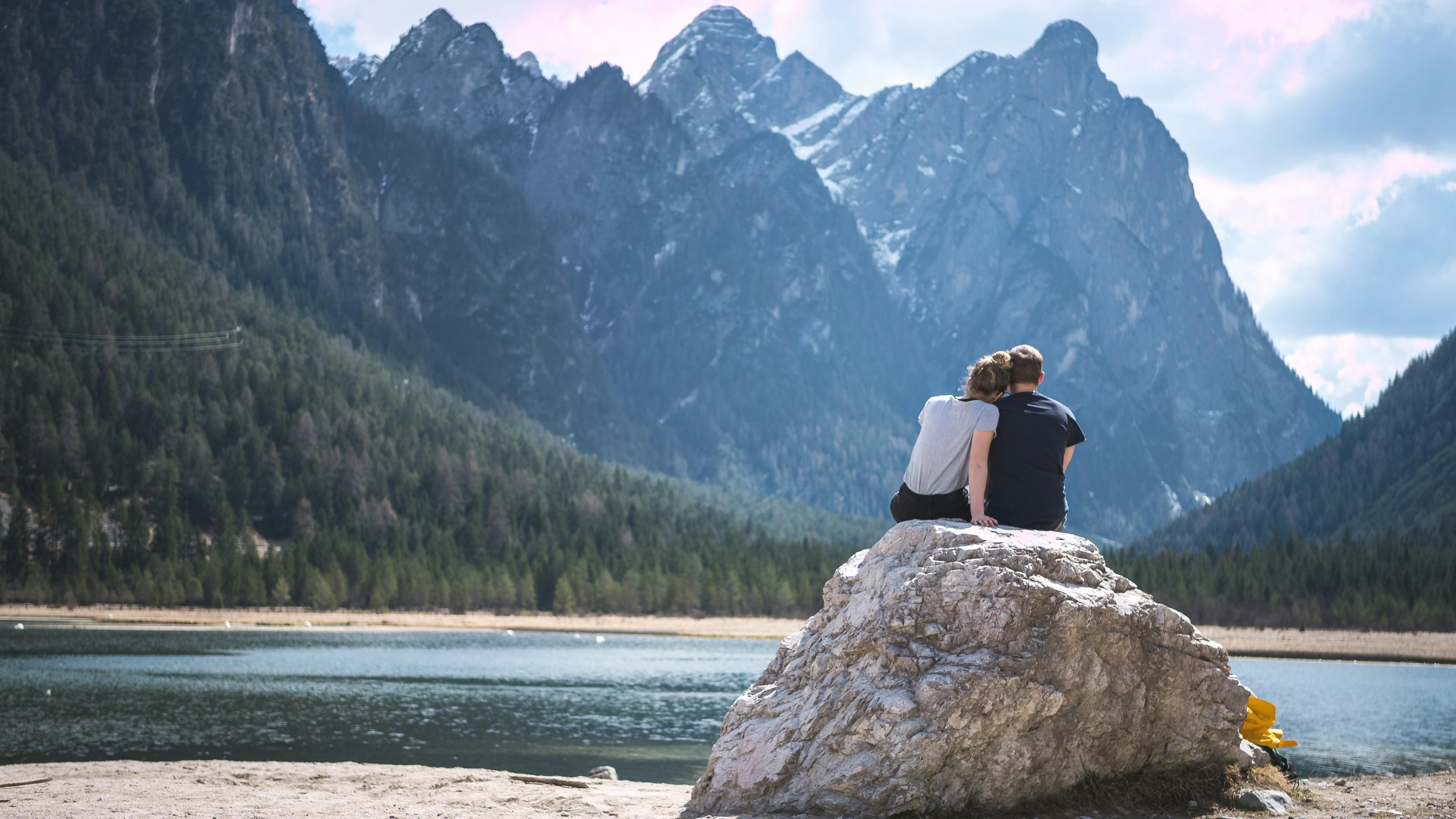 Couple sitting on a rock overlooking a mountain lake